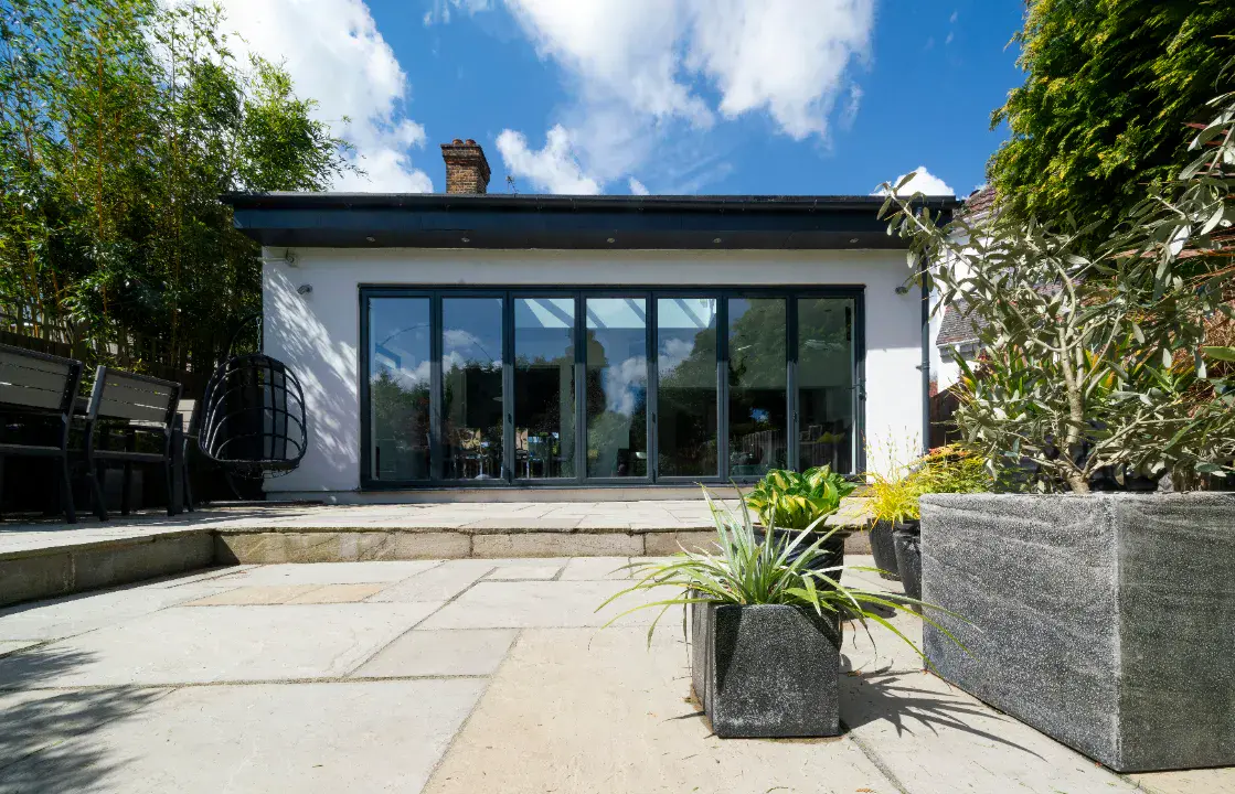 Modern garden room extension with white render, anthracite bifold doors and flat roof opening onto sandstone patio garden
