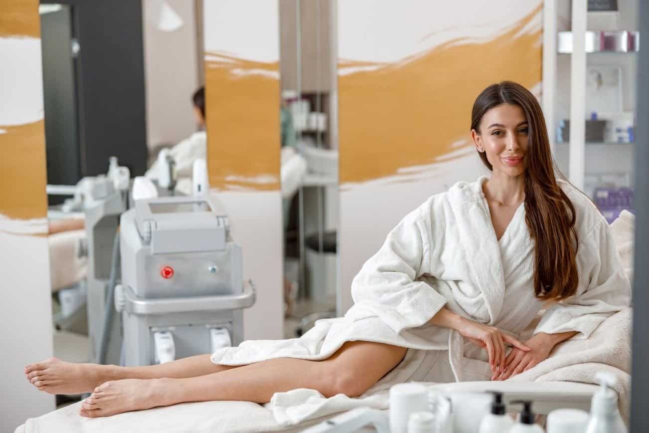 Woman relaxing in a Laser Spa Clinic before laser skin treatments, wearing a white robe next to a laser machine