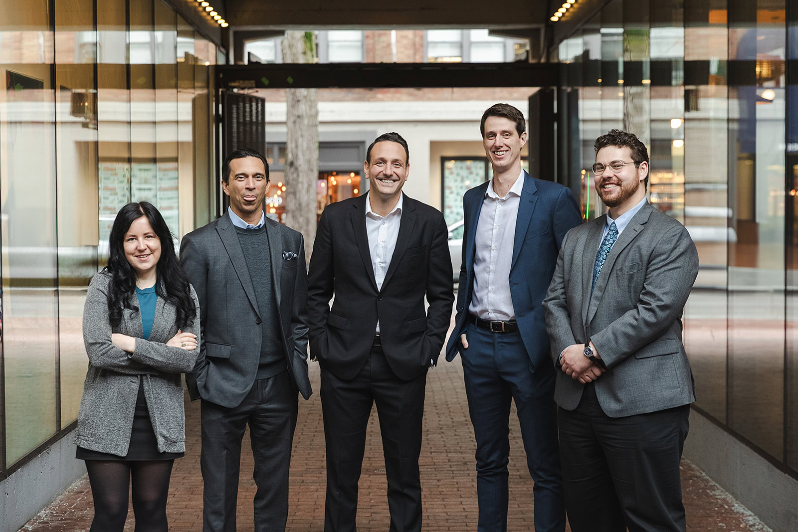 The Safe Pacific Financial team professionally dressed, three men in suits, one in a grey blazer, and one woman in a grey skirt and jacket, stand together outdoors, smiling in Gastown, Vancouver - ideal for discussing Infinite Banking or Whole Life Insurance Policy Loans.