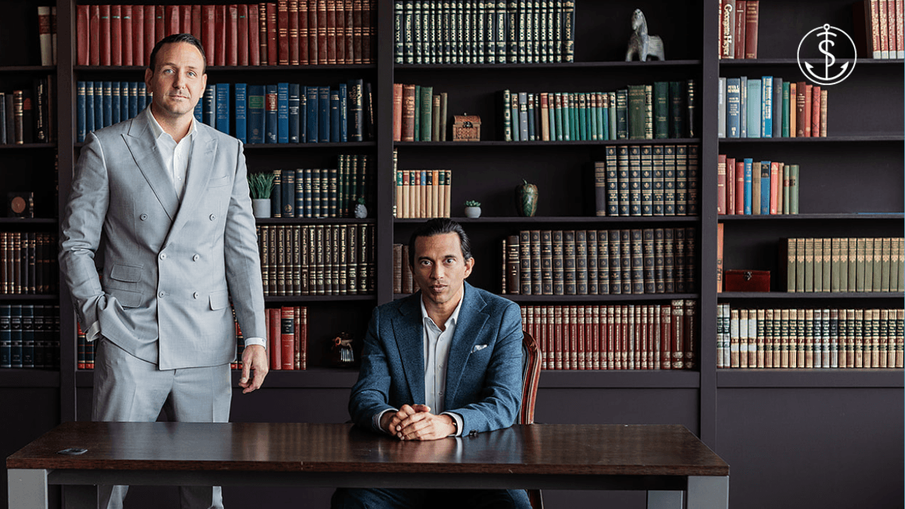 Robert Trasolini and Laurent Munier in suits, one standing and one sitting at a desk, pose in front of bookshelves filled with books in an elegant office or library setting, as a money symbol hints at whole life insurance in canada explained.