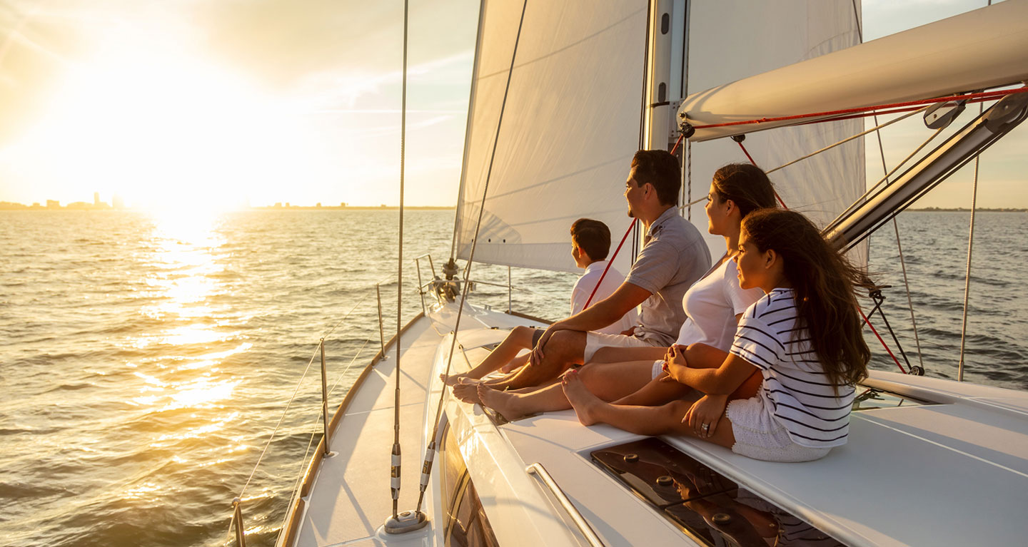 An affluent Canadian family of four enjoys sunset on a sailboat, discussing Safe Pacific wealth management and infinite banking.