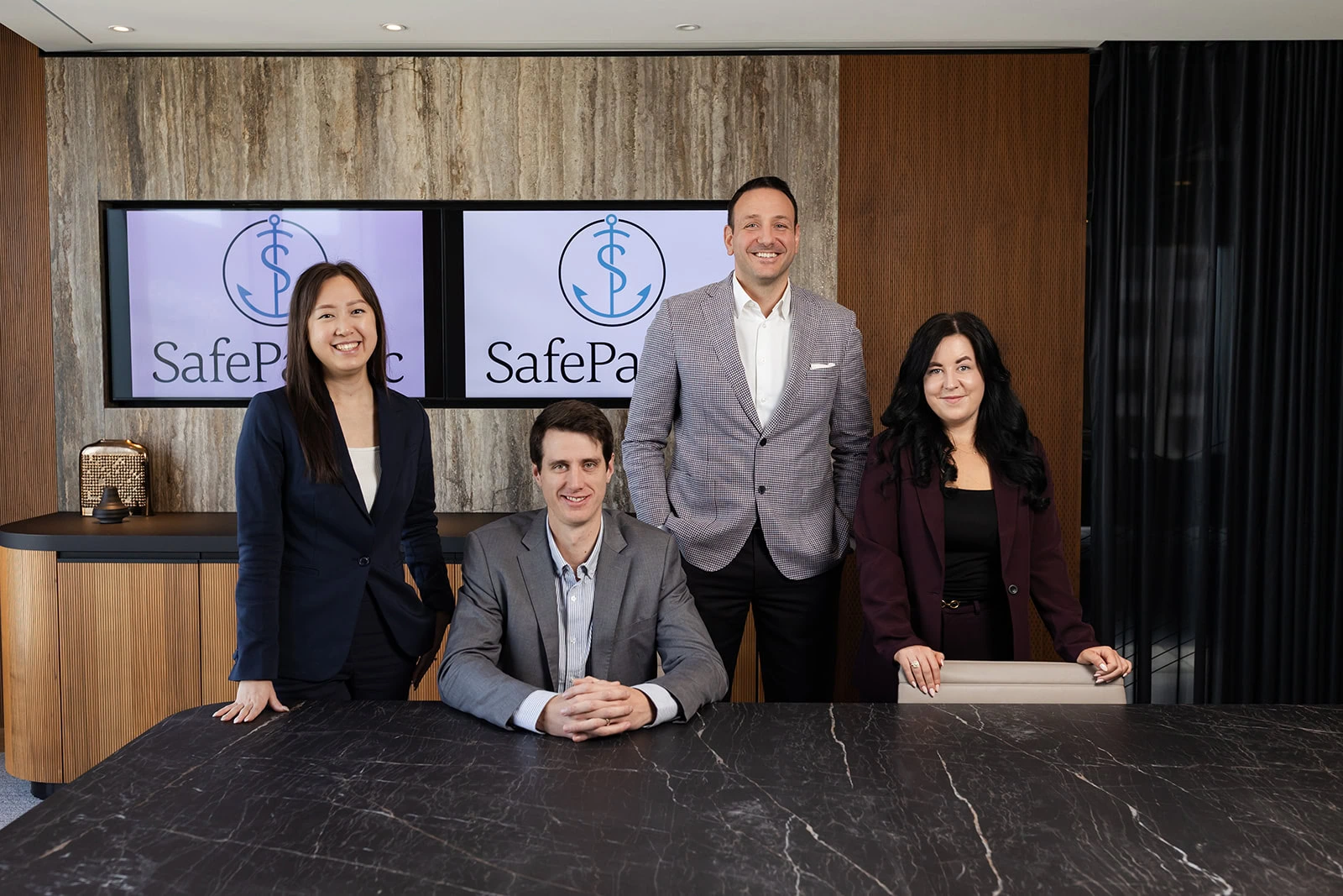 Four advisors at Safe Pacific Financial gather by a black marble table, with screens showing their bespoke wealth management solutions.