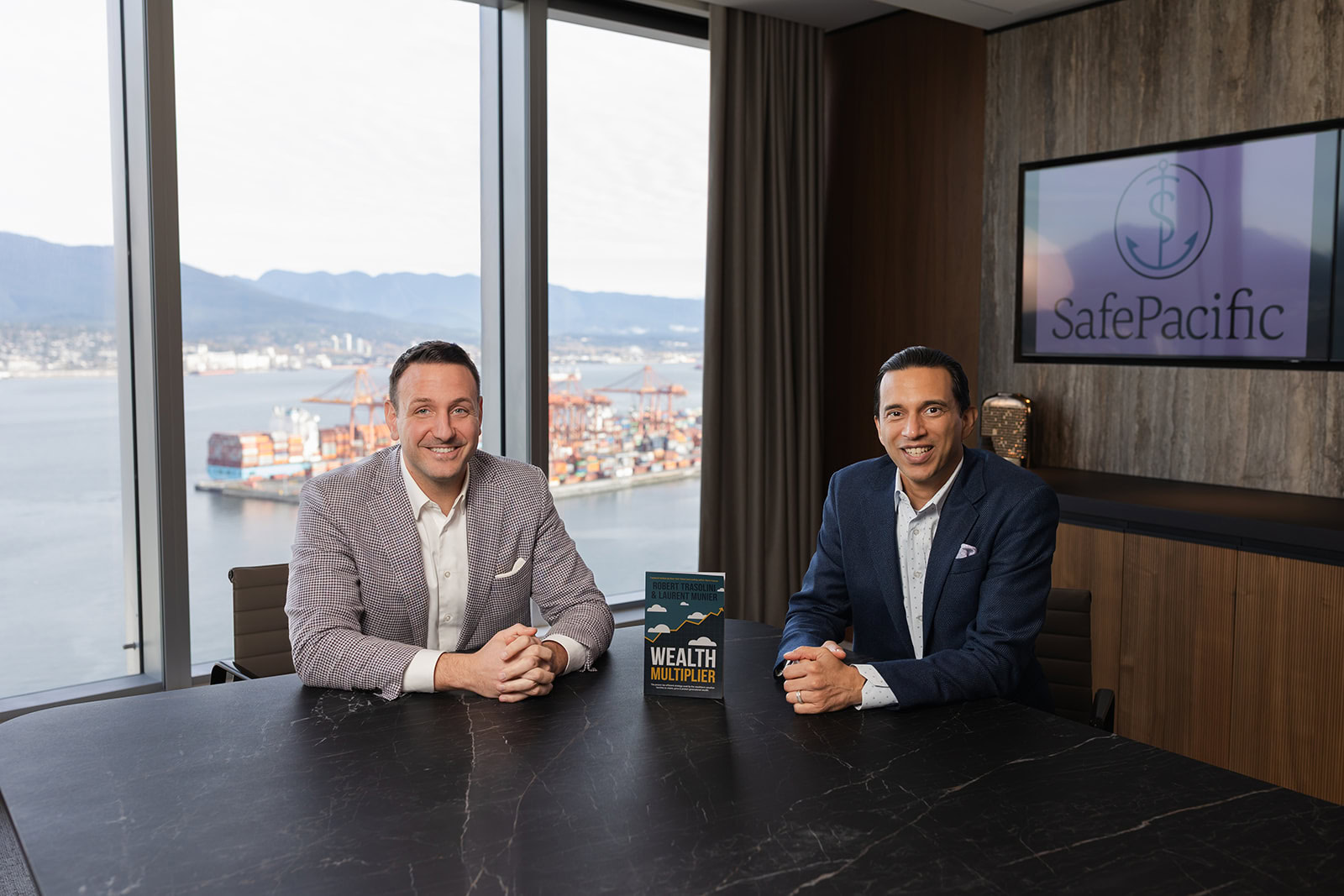 Two executives discuss wealth management and infinite banking at a Safe Pacific Financial meeting, life insurance book on table.