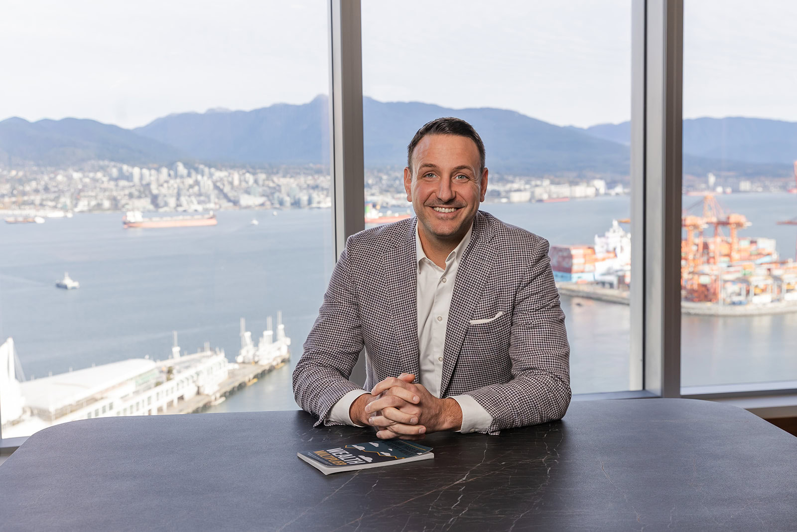 A client in a plaid jacket reviews Safe Pacific Financial’s wealth management magazine, smiling by harbor-view windows in Canada.