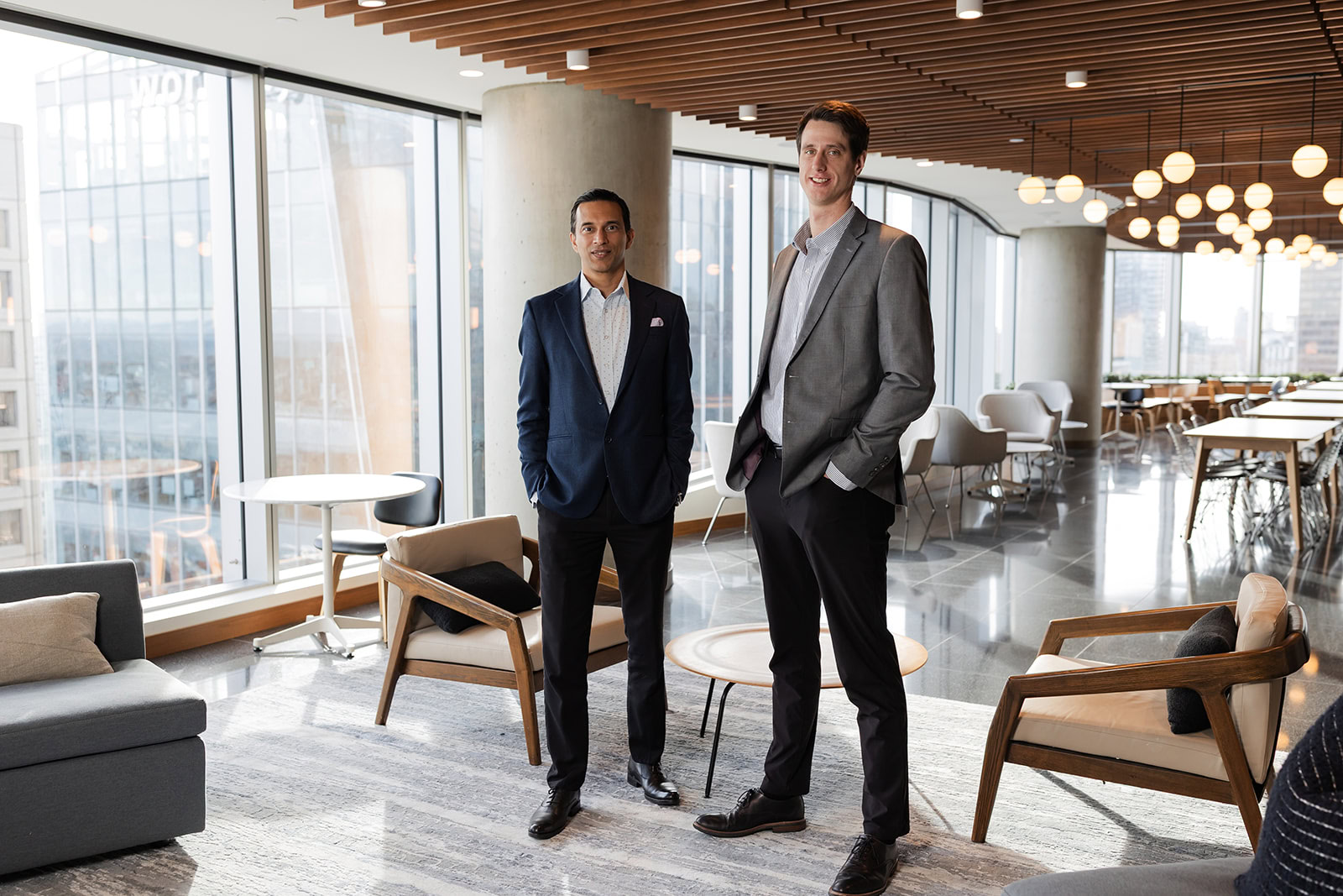 Two advisors discuss wealth management and infinite banking at Safe Pacific Financial's modern lounge, with city skyline views outside.