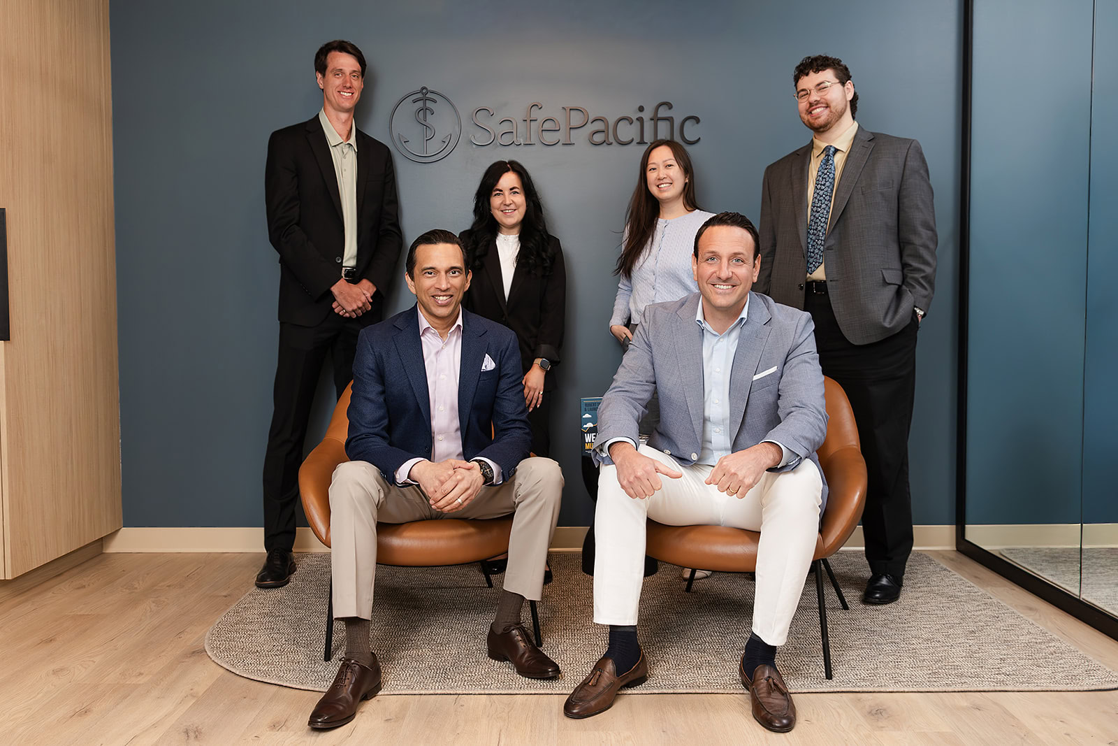 Six wealth advisors at Safe Pacific Financial smile in front of brand logo, experts in bespoke Canadian life insurance and infinite banking.
