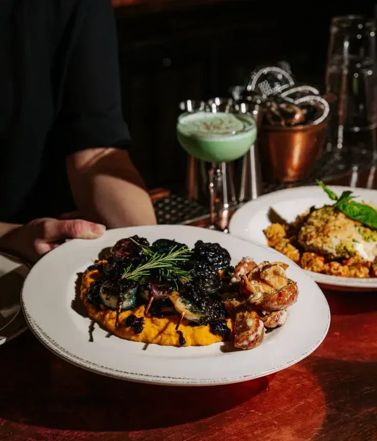 Server presenting a plated entrée at a dimly lit restaurant bar