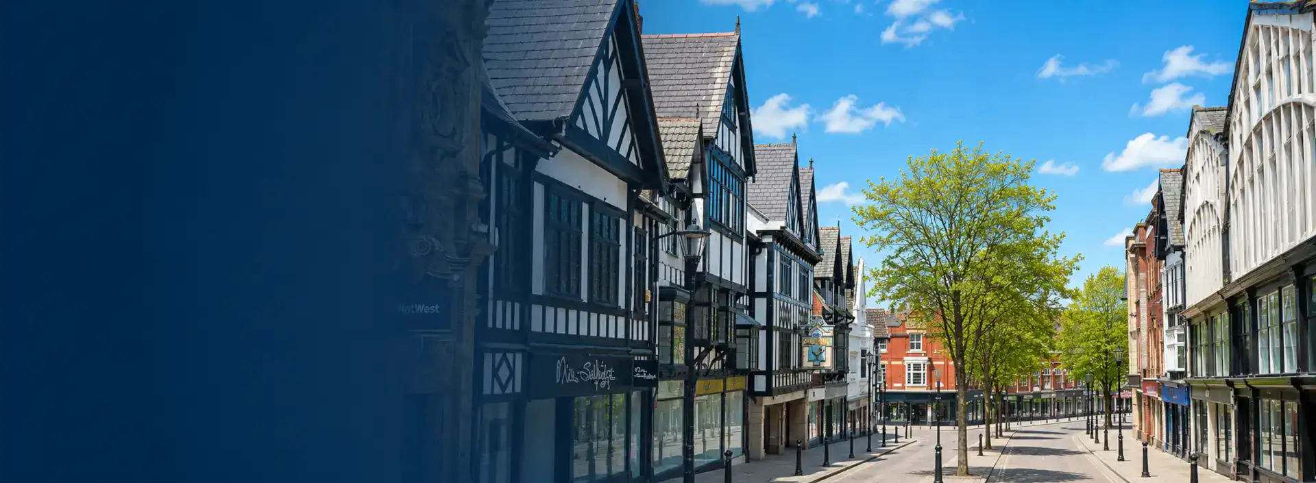 Home Improvements in Wigan banner showing a quiet town-centre street with traditional buildings and leafy trees on a bright summer day.