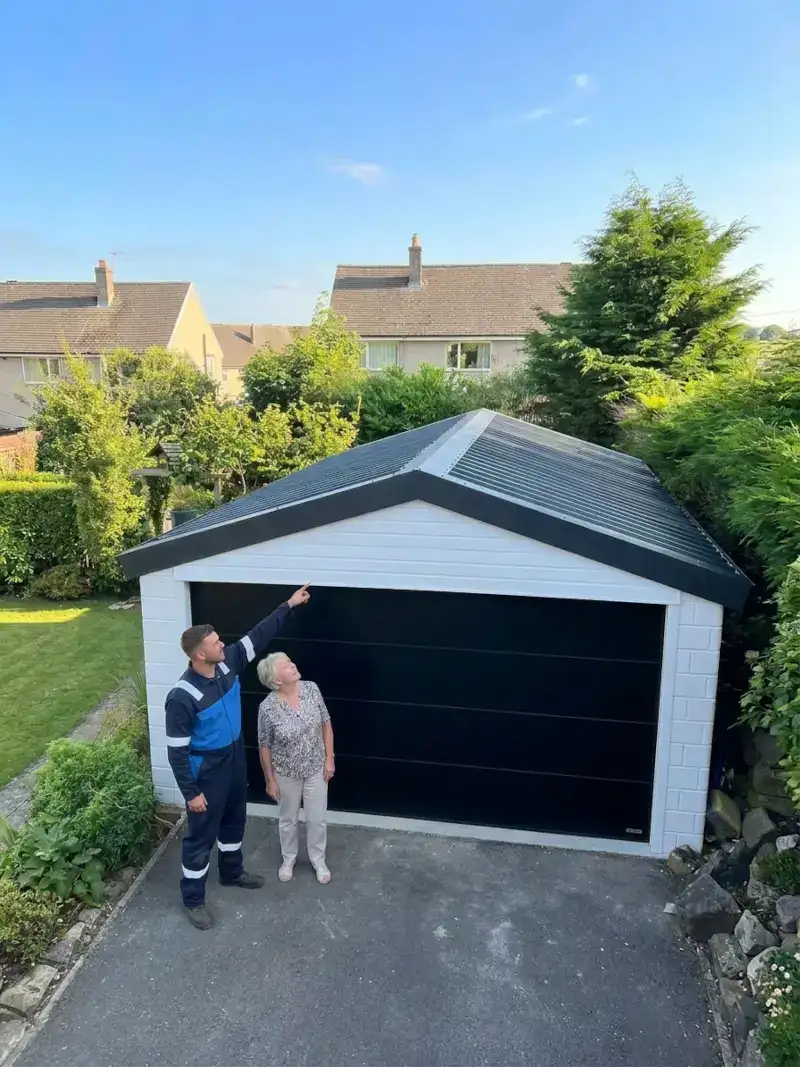 Garage roof replacement completion shown by a contractor pointing at the new metal roof to a smiling homeowner outside a white garage with a new black door.