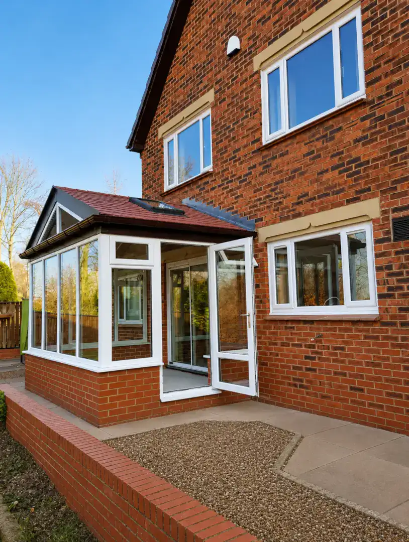 White uPVC conservatory attached to a red-brick home with clean brickwork and dry paving.