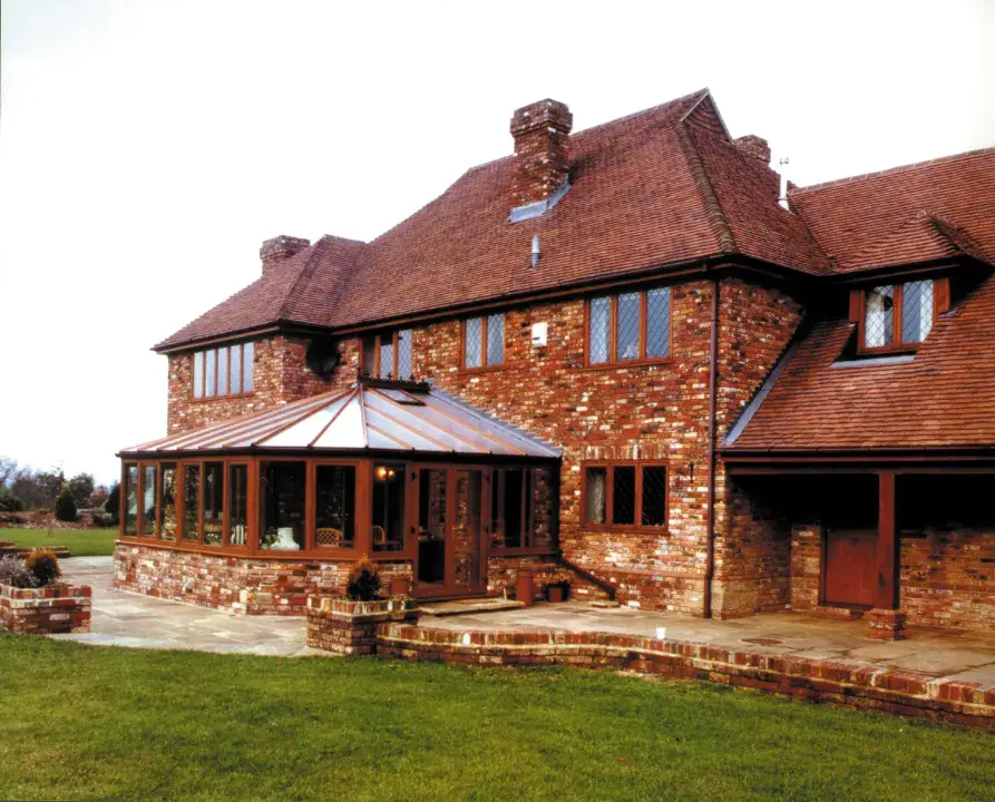 Brown Victorian conservatory attached to a traditional brick house with matching roof and paved terrace.