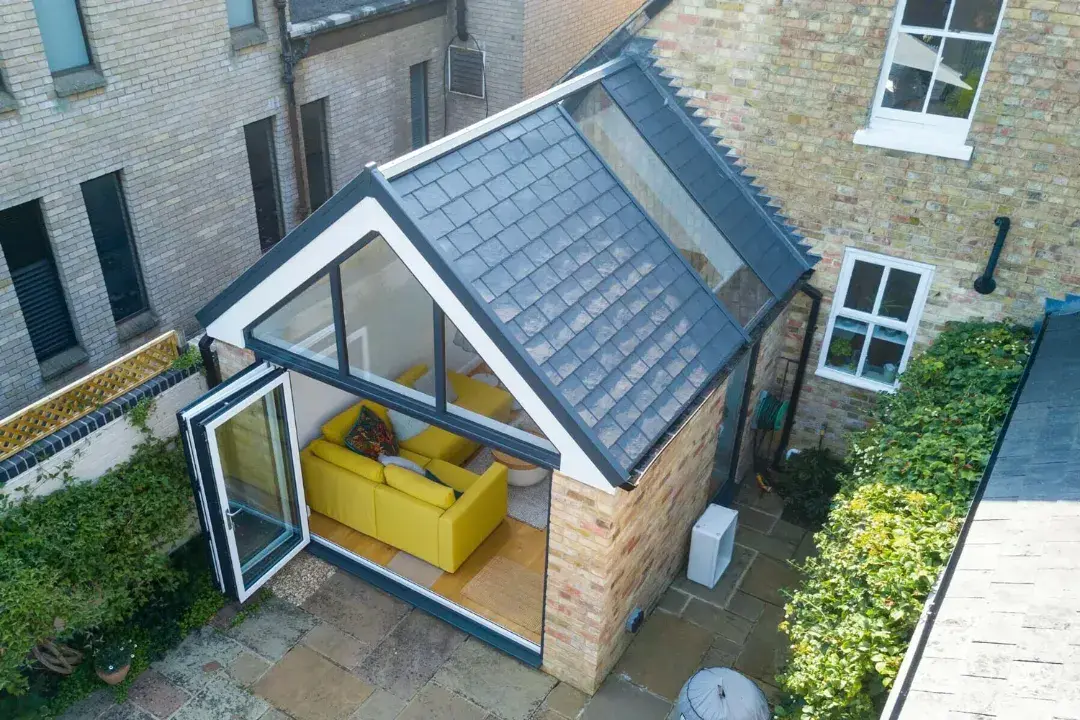 Aerial view of a tiled conservatory roof with gable glazing, bifold doors and a yellow sofa inside.