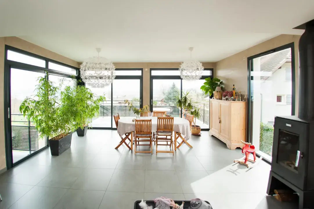 Black aluminium sliding patio doors surrounding a bright dining room with tiled floor, plants and large garden views.