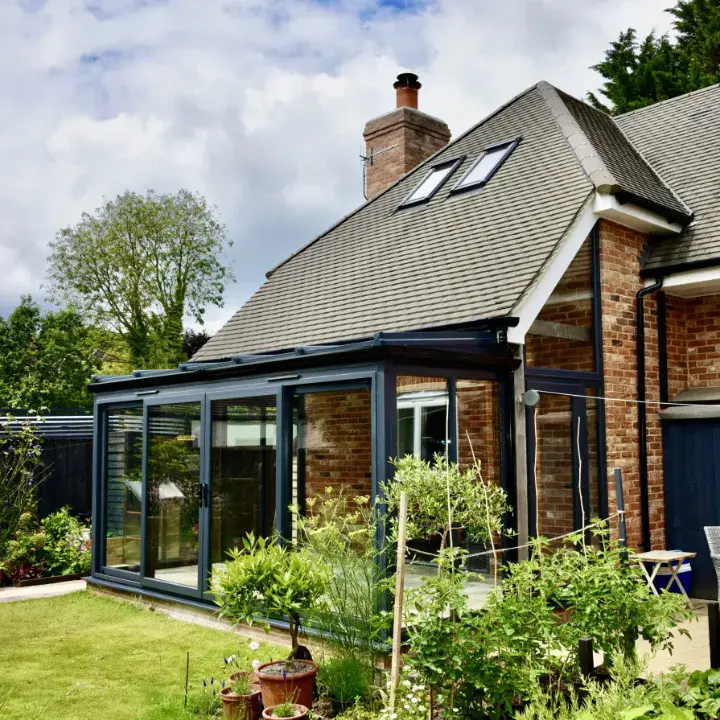 Brick lean-to conservatory with dark frames, full-height glazing and garden-facing sliding doors.