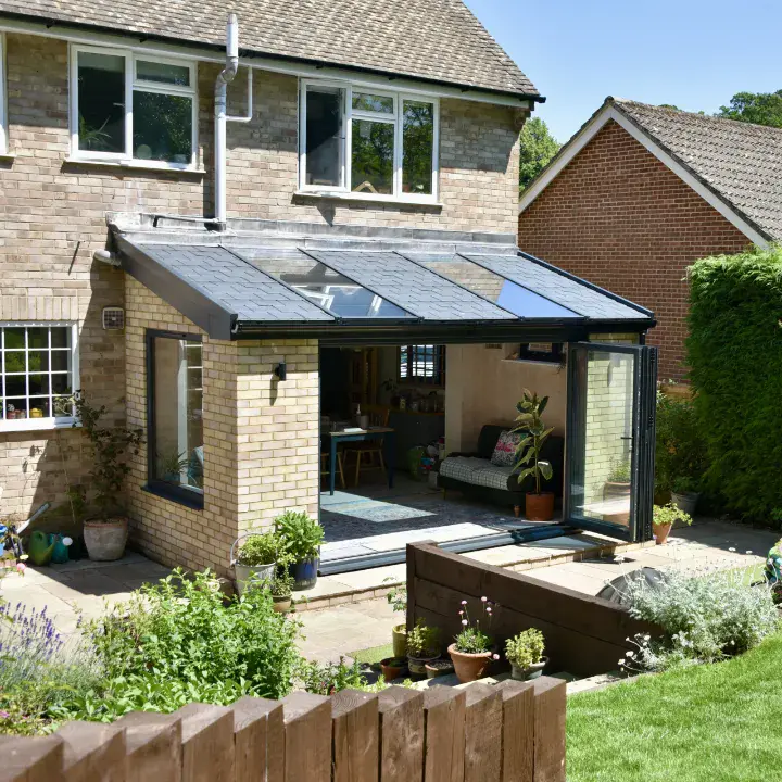 Lean-to conservatory with a tiled roof, roof windows, dark sliding doors and brick pillars opening onto a garden patio.