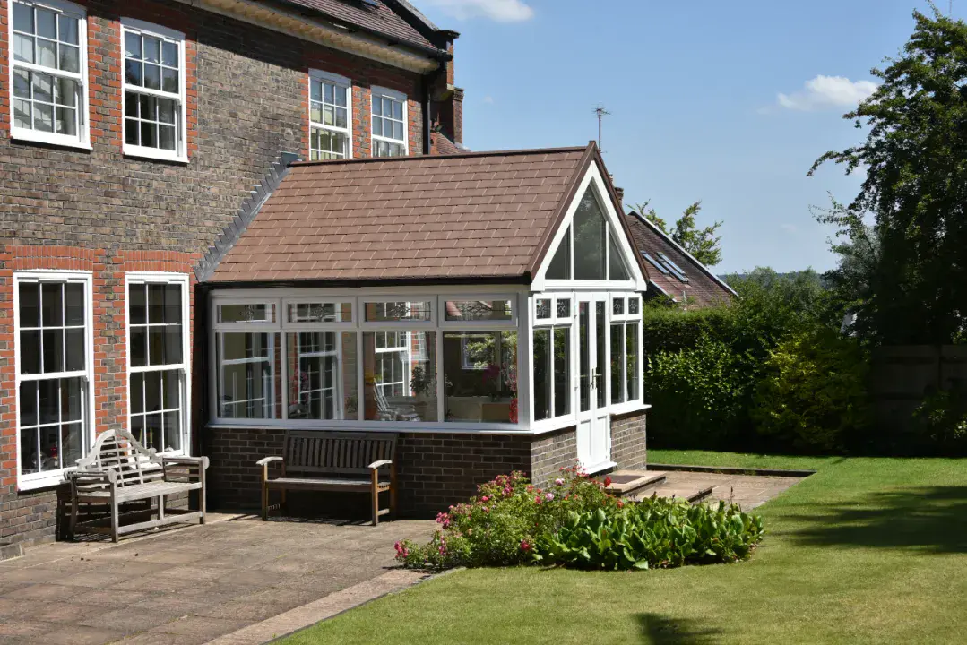 Traditional gable end conservatory with white frames, tiled roof and French doors facing a lawn garden.
