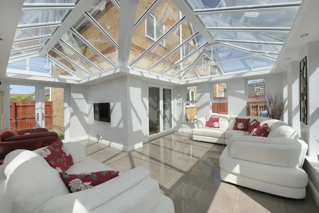 Bright combination conservatory with multiple glazed roof sections, white sofas and polished tiled flooring.