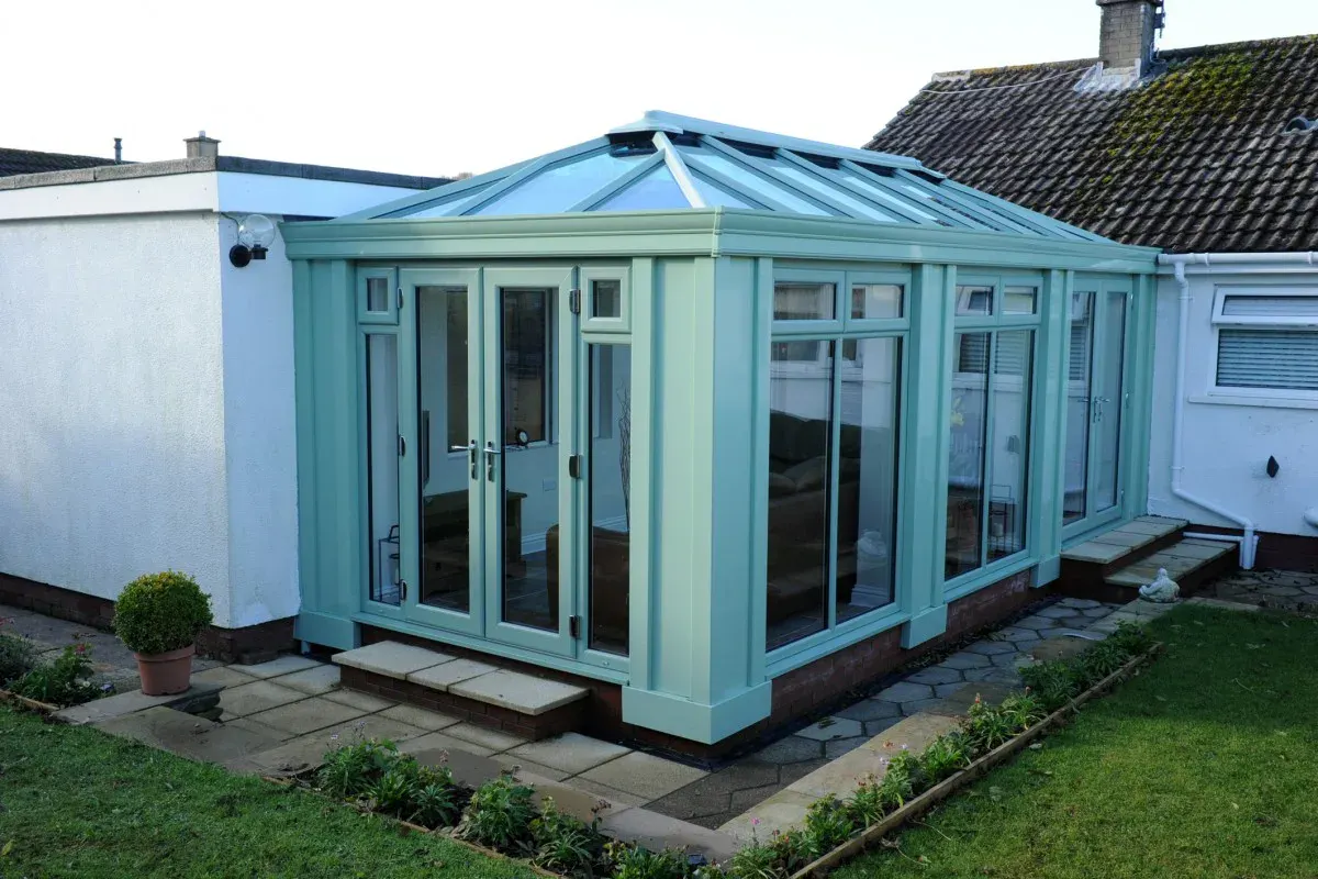 Pale green orangery kitchen extension with a glazed roof, French doors and garden patio access.