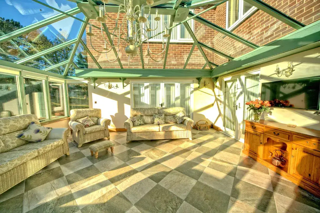 Combination conservatory interior with green roof framing, glass ceiling, wicker sofas and chequered tiled floor.
