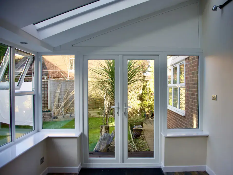 Lean-to conservatory interior with white French doors, side windows and a sloped ceiling leading out to the garden.