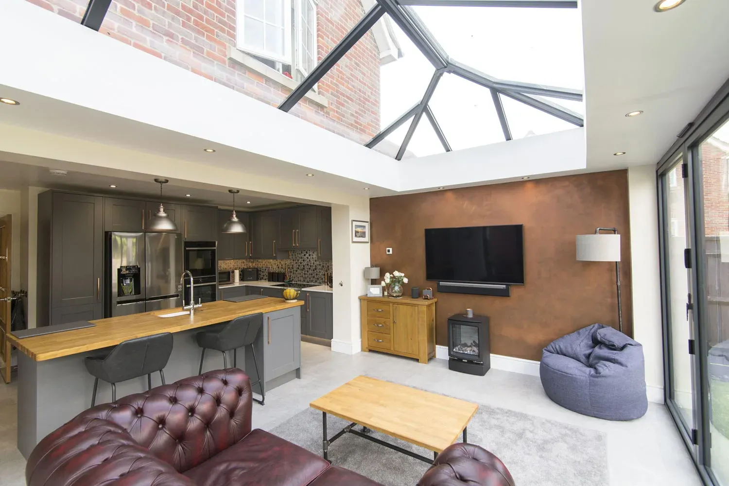 Open-plan orangery kitchen extension with grey cabinets, timber island, roof lantern and lounge area.