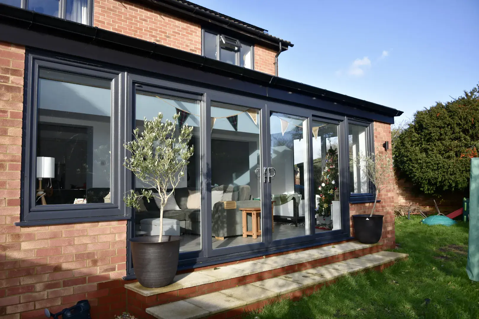 Red brick orangery with dark grey frames, full-height doors and a garden-facing glazed roof lantern.