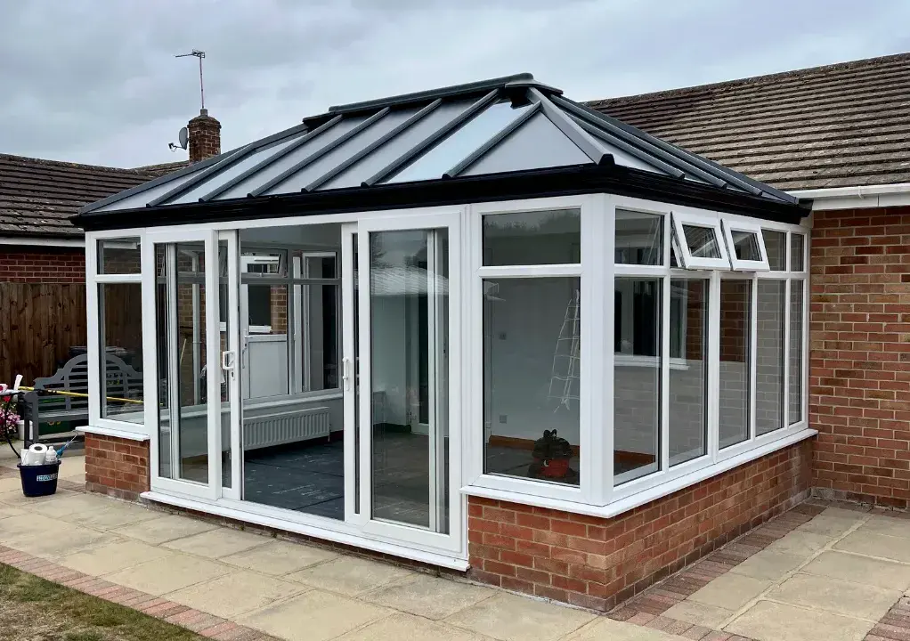 White conservatory with solid roof panels, brick base, French doors and opening side windows.