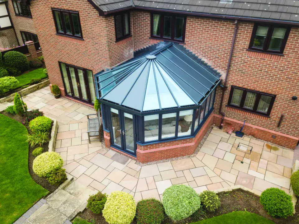 Aerial view of a solid roof conservatory with dark frames, brick base and shaped patio beside a red brick house.