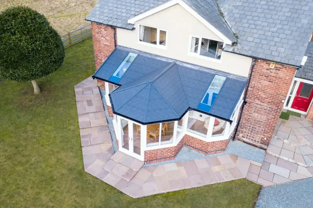 Aerial view of a T-shaped conservatory with a tiled roof, roof windows and brick base attached to a country house.