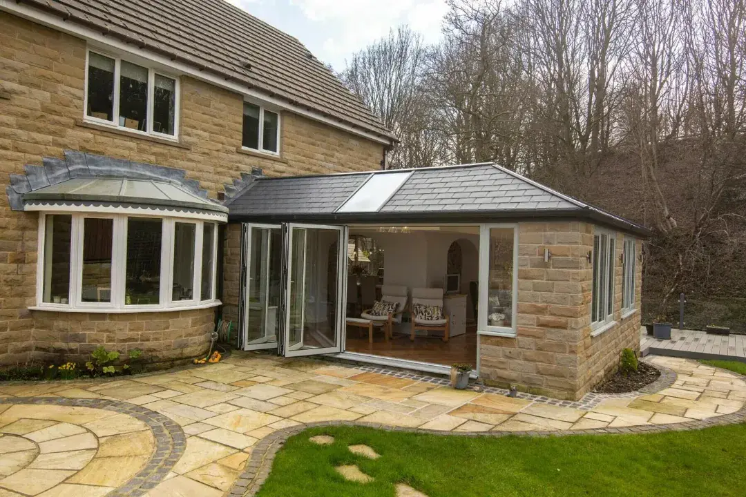 Tiled conservatory roof extension with wide open bifold doors, stone walls and a curved garden patio.