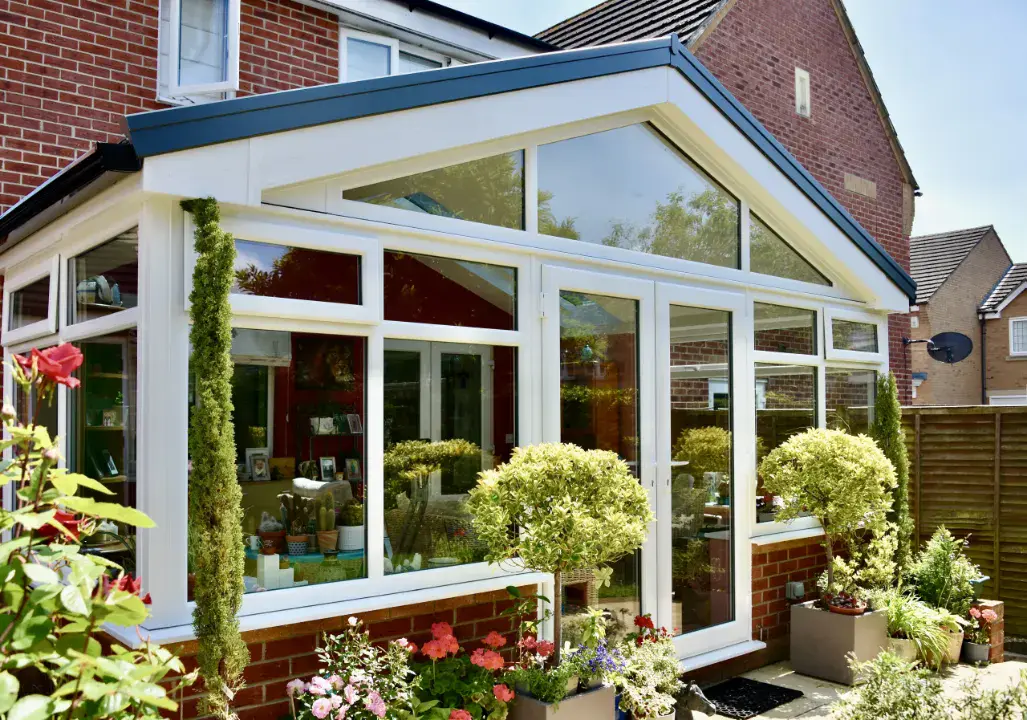 White gable end conservatory with large glazed panels, brick dwarf wall and landscaped planters outside.