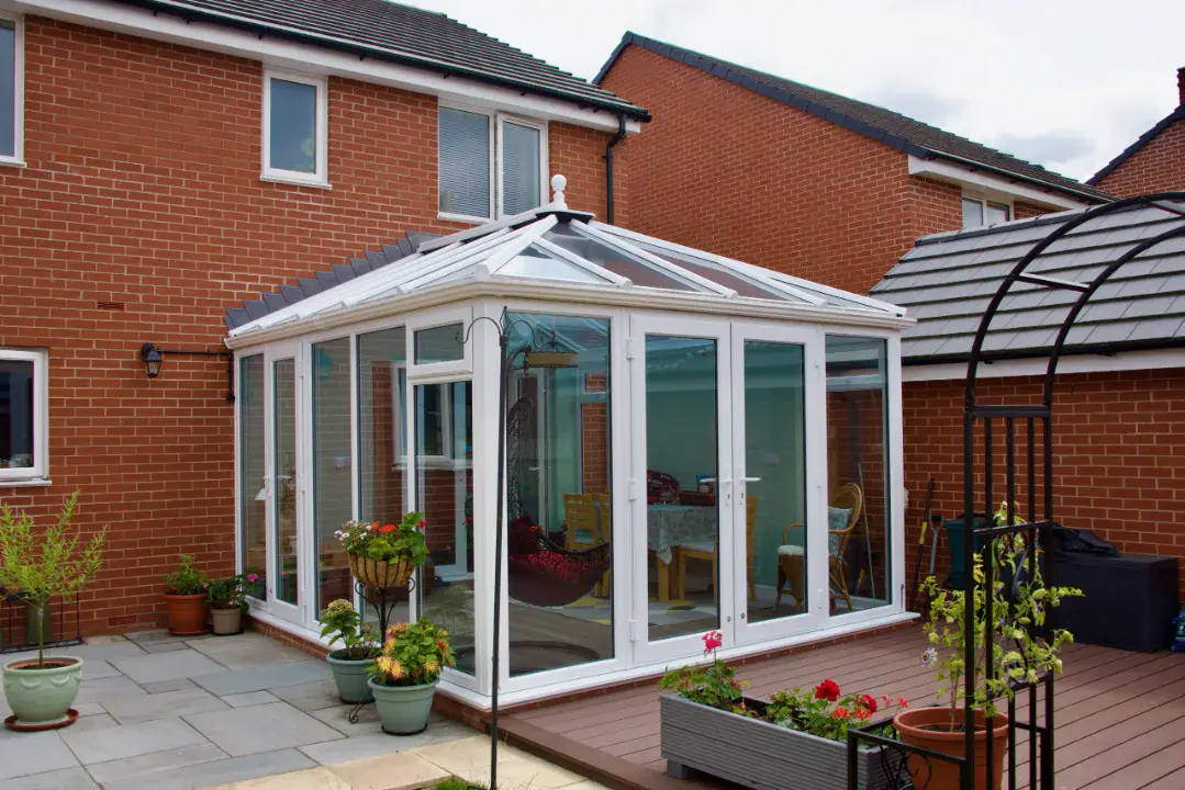 White framed Edwardian conservatory with glass doors, glazed roof and patio garden area.