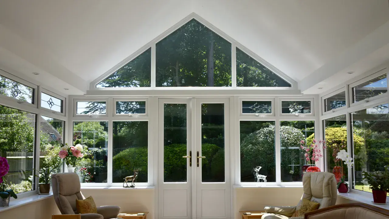 Inside a white gable end conservatory with triangular glazing above French doors and views of the garden.