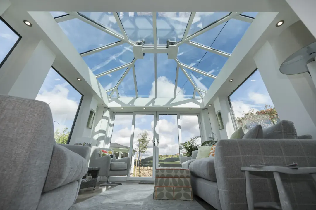 White glass conservatory roof viewed from inside, with sofas, garden doors and open countryside beyond.