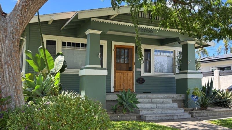 North Park San Diego Craftsman bungalow near Morley Field with a covered front porch, green siding, wood front door, and drought-tolerant landscaping.