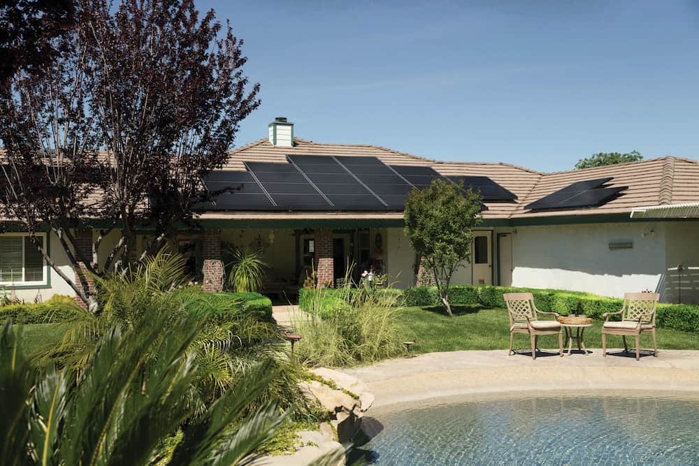 Beautiful backyard featuring a sparkling swimming pool, lush landscaping, and solar panels on the roof by Vivint Solar from Pexels