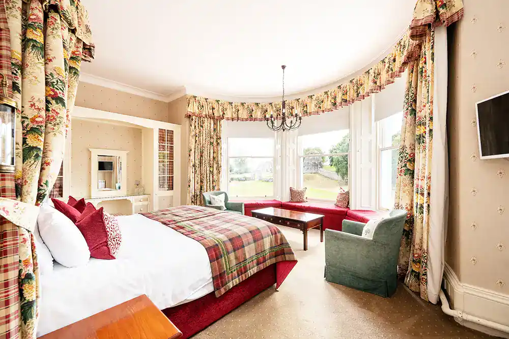Elegant bedroom with plaid bedspread, large windows and floral curtains.
