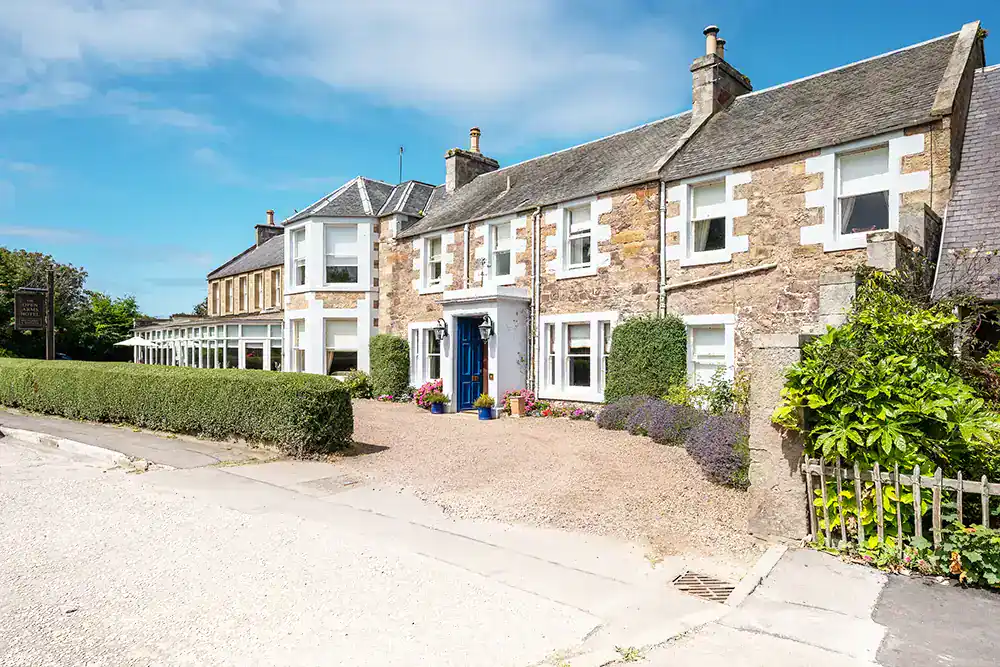 Stone house with blue door, white-trimmed windows, hedges, and gravel driveway.