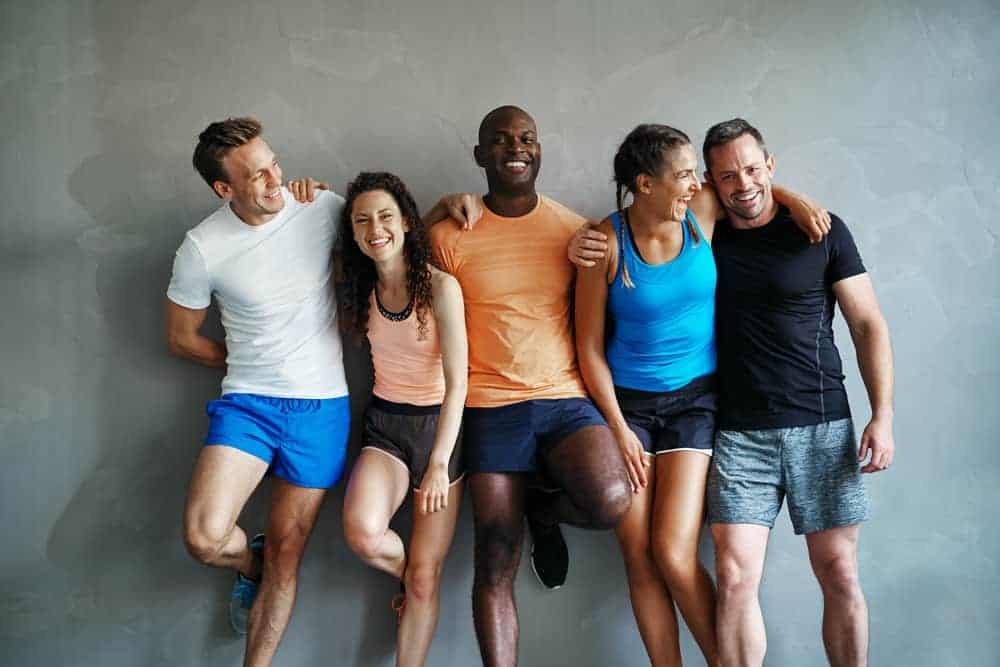 Two women and three men leaning against a wall smiling