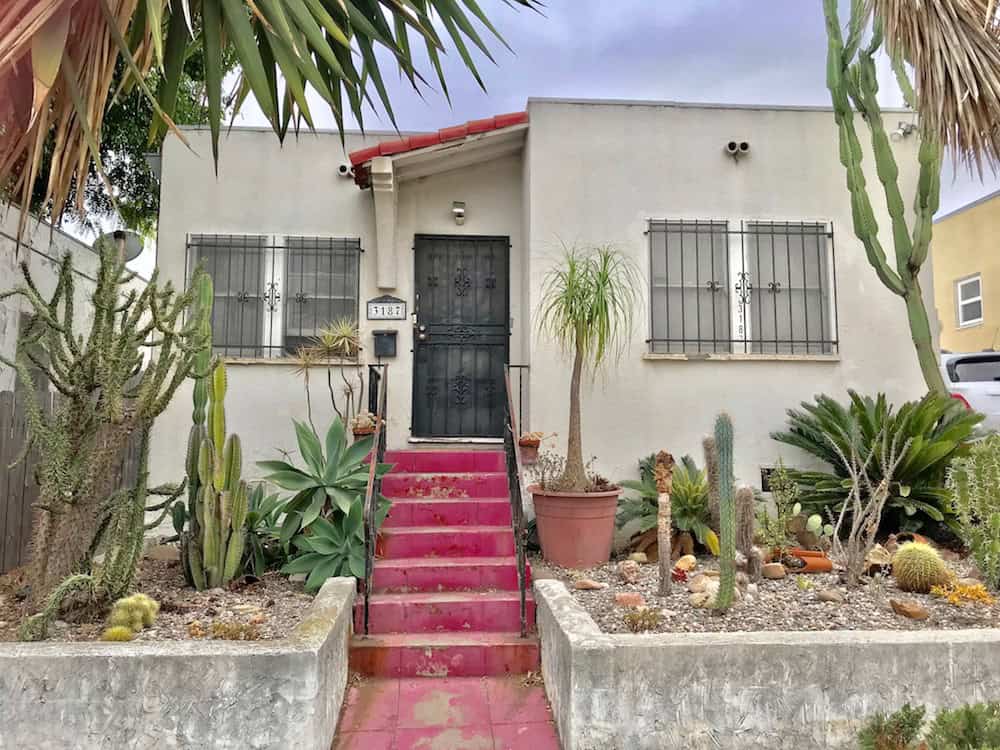 Street view of the Spanish-style cottage at 3187 Lincoln Ave in North Park featuring vibrant pink exterior stairs, desert landscaping with various cacti and succulents, and a security screen door.