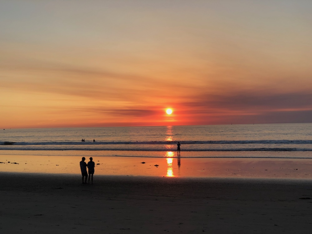 Sunset at Pacific Beach, San Diego with silhouettes of people on the shore and golden reflections on the water
