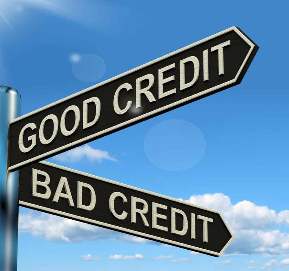 Two black directional street signs against a bright blue sky with clouds, one pointing up toward "GOOD CREDIT" and the other pointing down toward "BAD CREDIT."