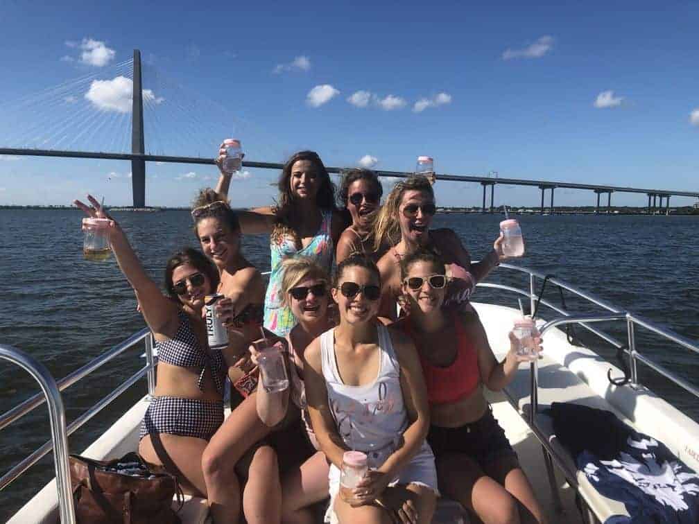 Group of women cheering with their drinks on the boat in front of the bridge. Charleston booze cruise bachelorette