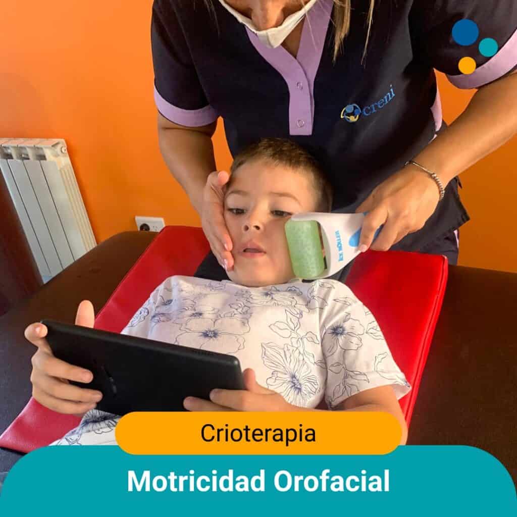 Niño mirando la tablet mientras la fonoaudióloga le pasa un rodillo a bajas temperaturas.