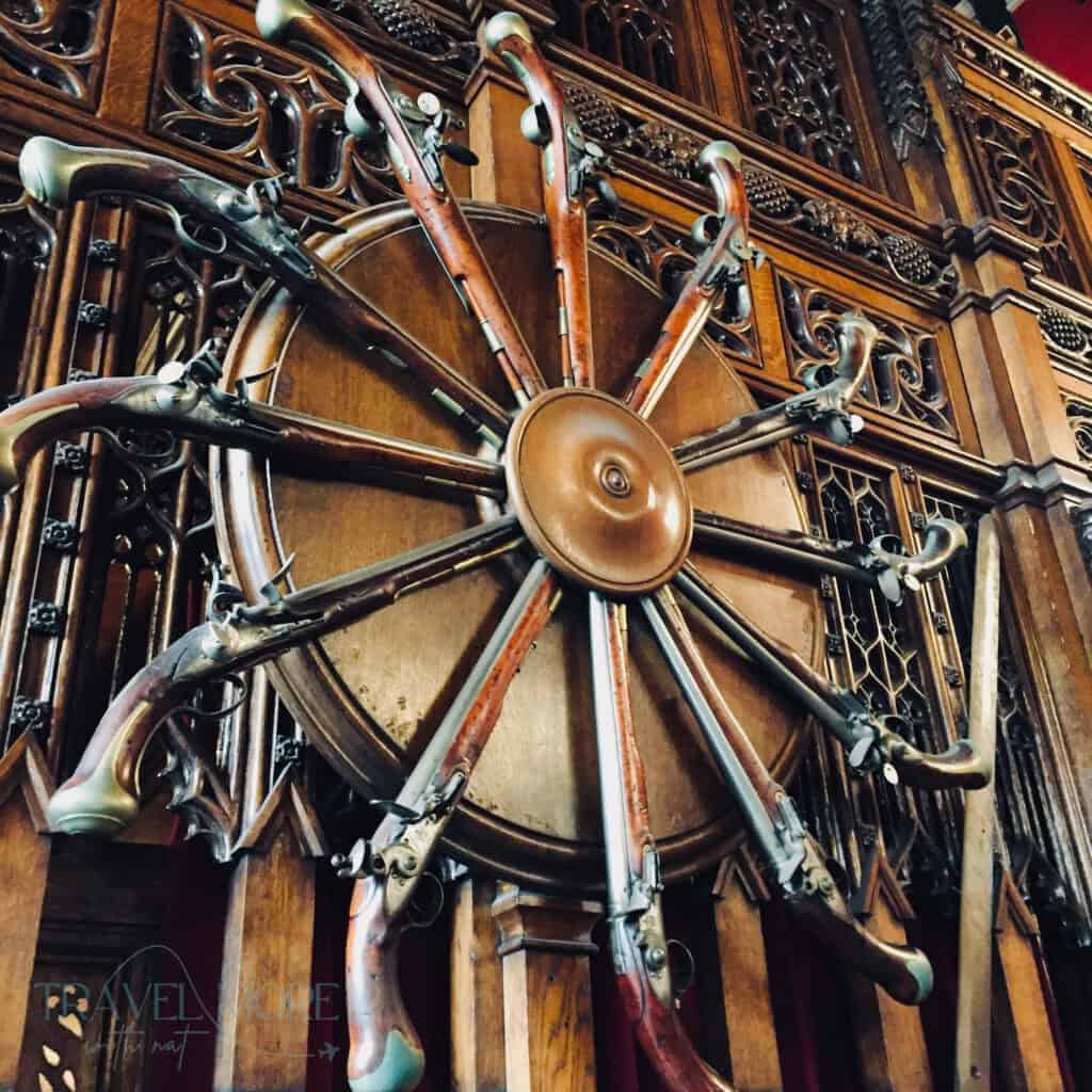 Decorative circular display of antique pistols mounted on carved wooden paneling inside the historic Edinburgh Castle attraction.