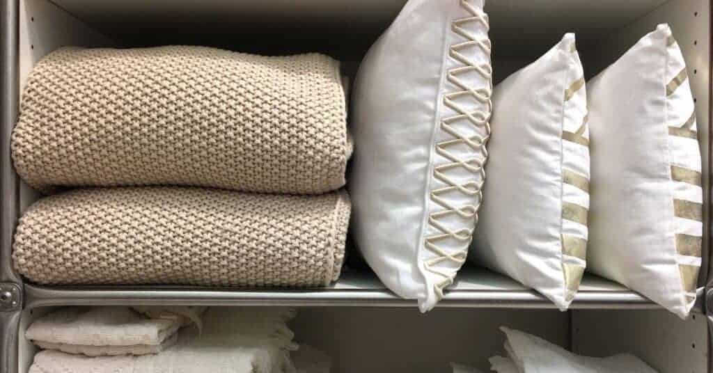 Blankets and pillows stored on linen closet shelves