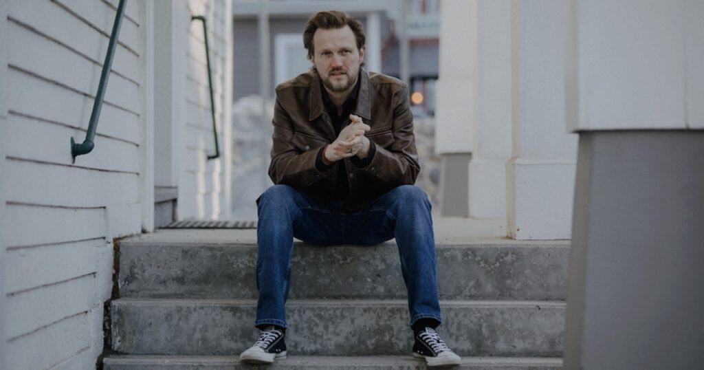 Man sitting on outdoor concrete steps, casual streetwear, urban setting, thoughtful expression, young adult male, modern lifestyle, city background.