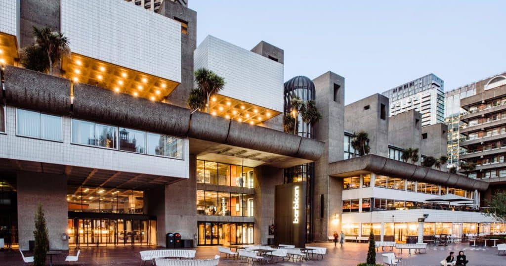 Modern urban building with glass windows, outdoor seating, and warm lighting, highlighting architecture and cityscape, perfect for music industry events, creative hubs, or entertainment venues.