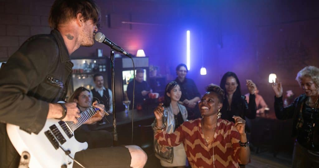 Live music performance at a vibrant nightclub with an enthusiastic audience enjoying the artist's guitar and singing, creating a lively and energetic atmosphere.