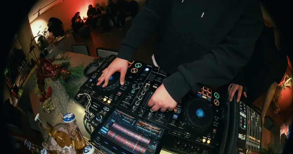 1. DJ miksa glazbu na događaju uživo s profesionalnom opremom, osvijetljen šarenim svjetlima, u živopisnom noćnom klubu ili koncertnom okruženju.